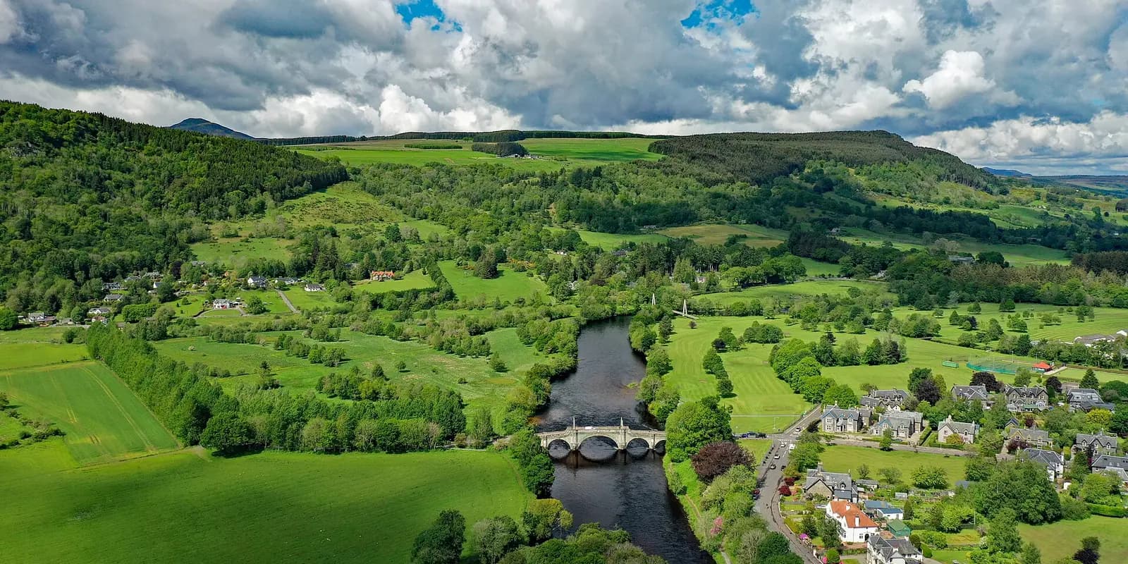 Aberfeldy from the air: the old stone bridge over the River Tay, with fields and wooded hills around the town