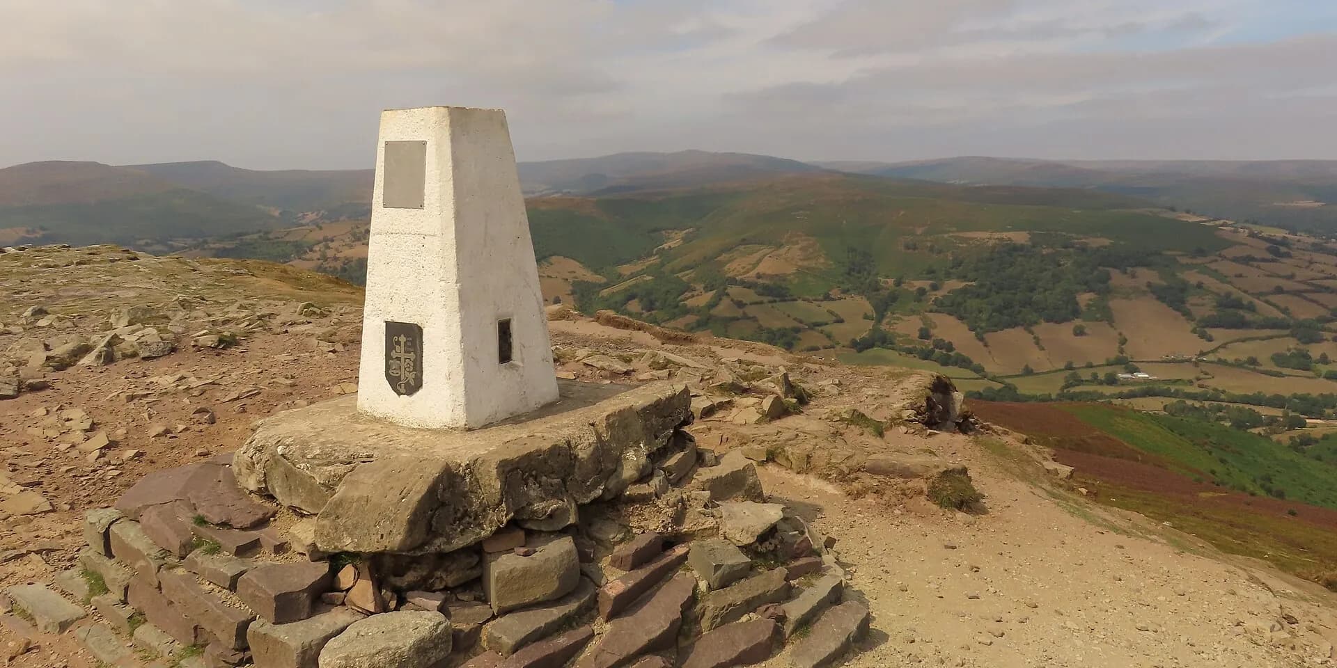 The stone trig point on the summit of the Sugar Loaf, with hills and valleys stretching away below