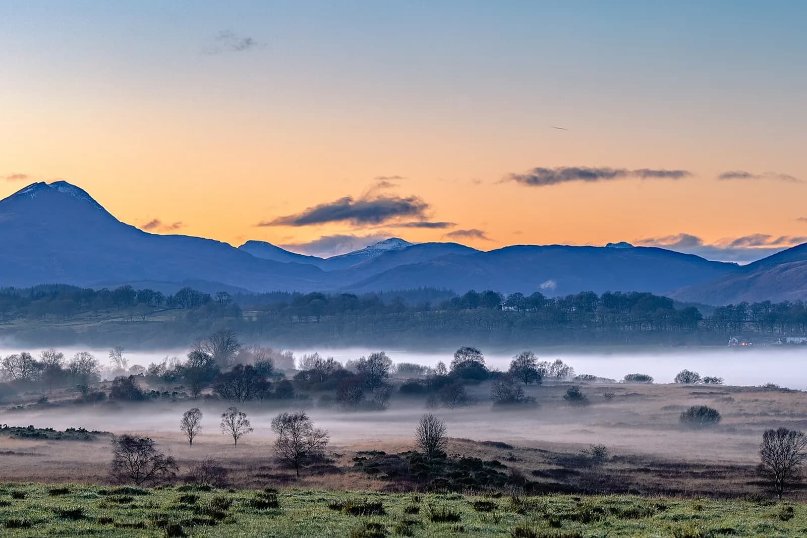 Ben Lomond silhouetted against a sunset sky, with mist lying over the fields below