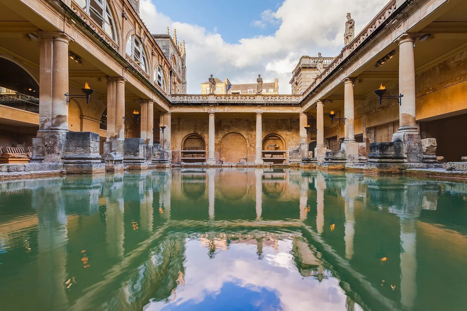 The green water of the Great Bath at the Roman Baths, surrounded by stone columns and statues