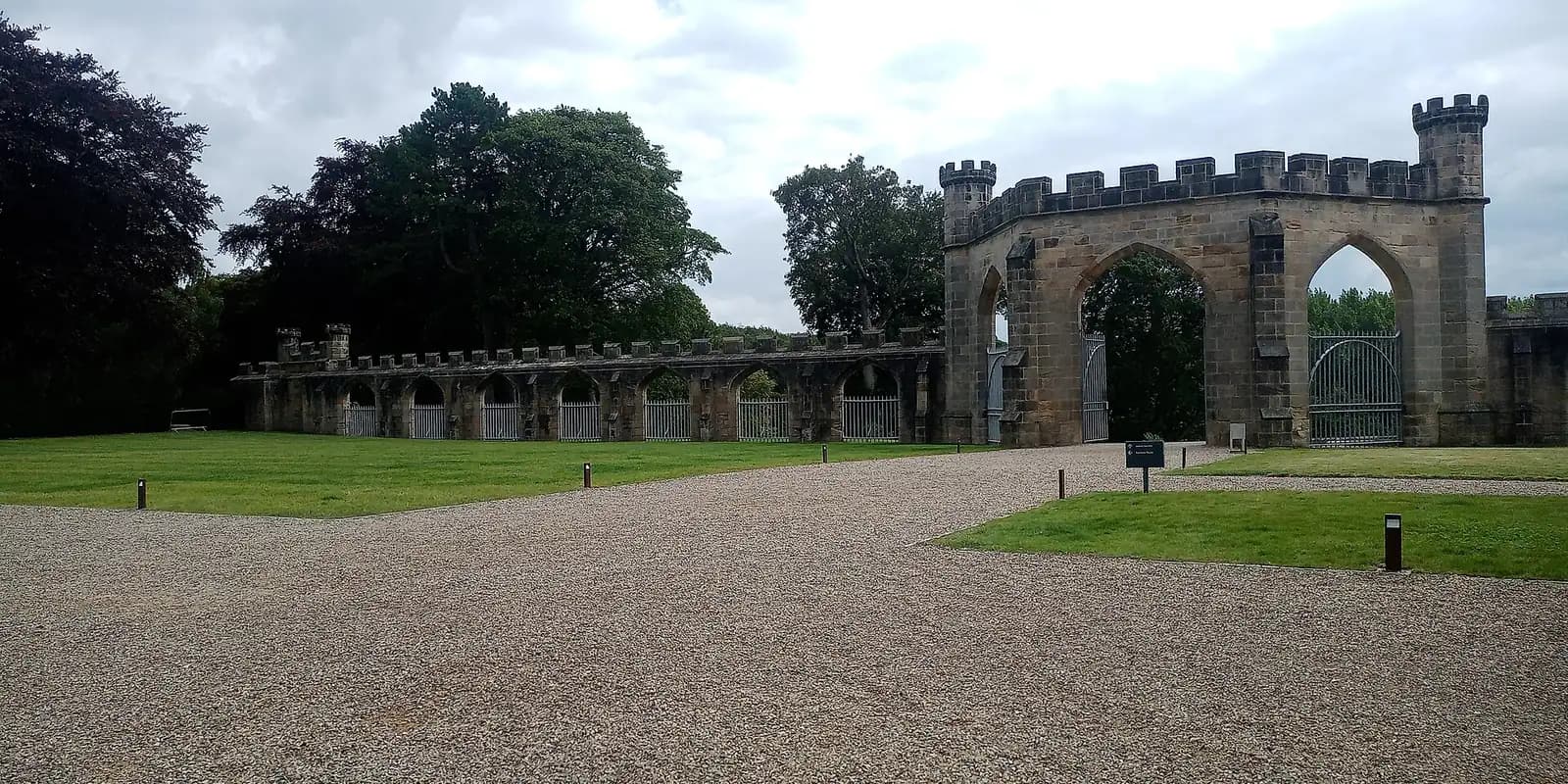 The battlemented stone screen wall and gateway of Auckland Castle, beside a lawn and trees
