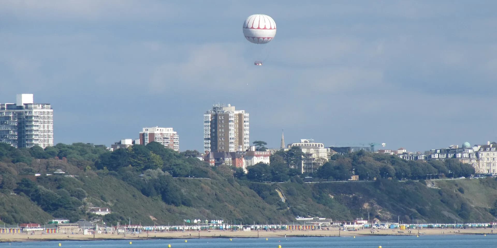 Bournemouth's long sandy beach and cliff-top buildings seen from across the bay, with a tethered balloon in the sky