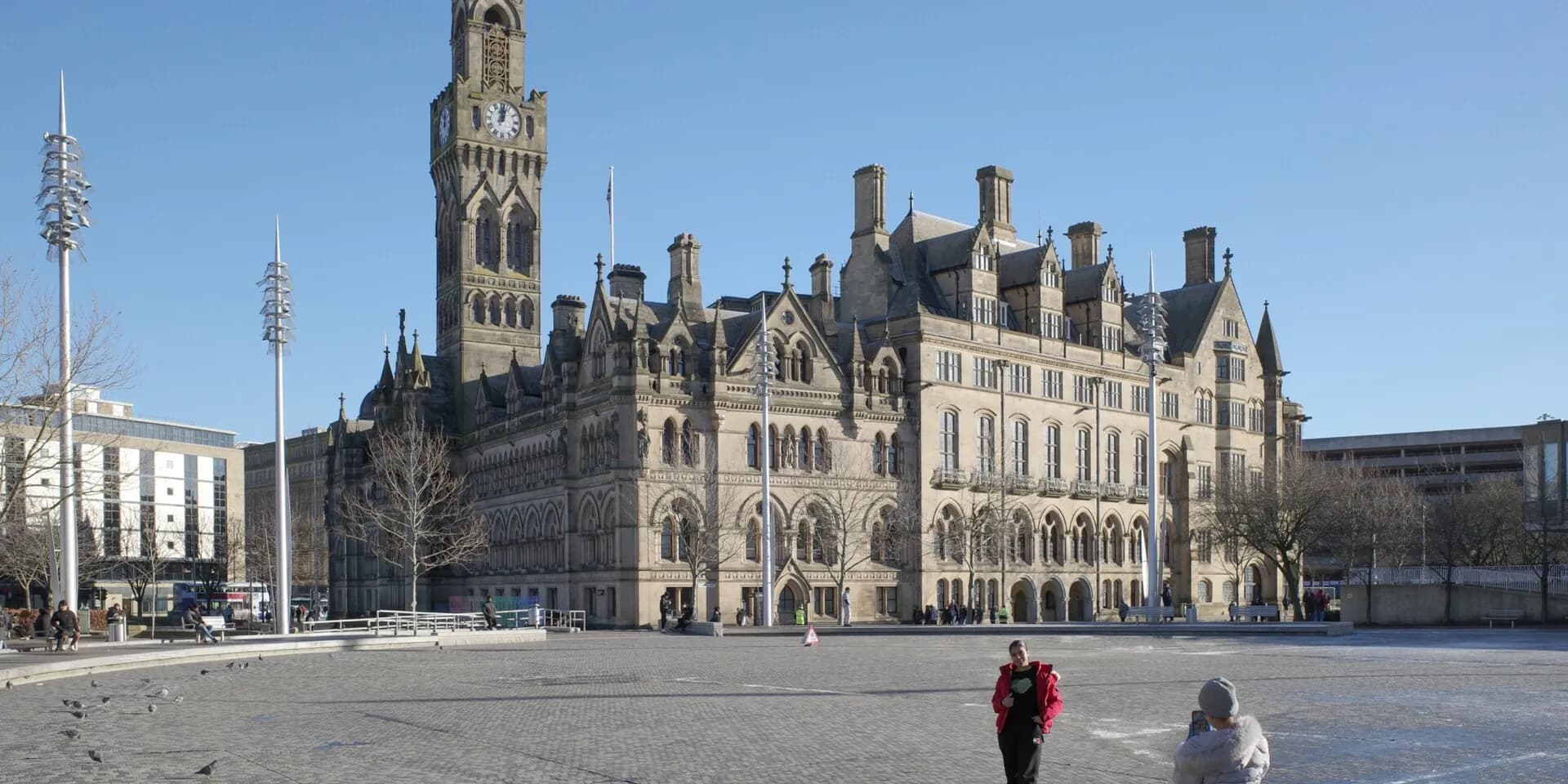 Bradford City Hall, a grand stone building with a clock tower, across the open square of City Park
