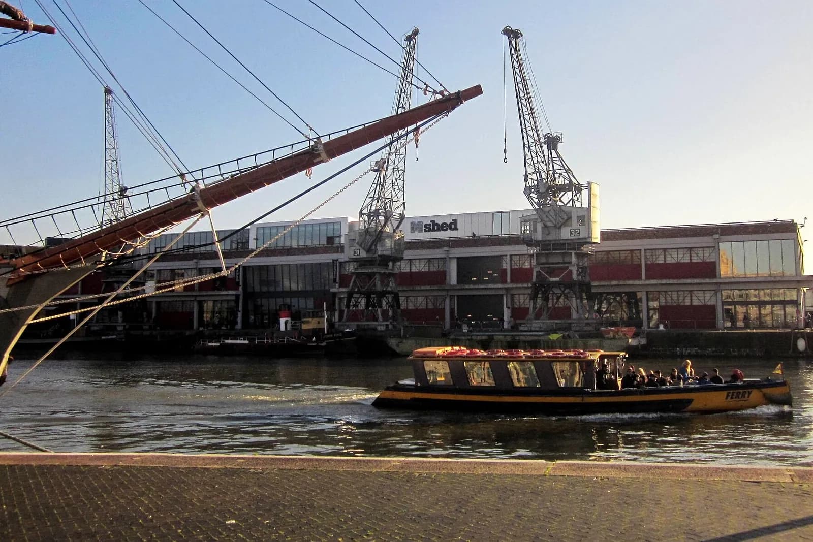 A small ferry crossing Bristol's Floating Harbour past the dockside cranes at M Shed
