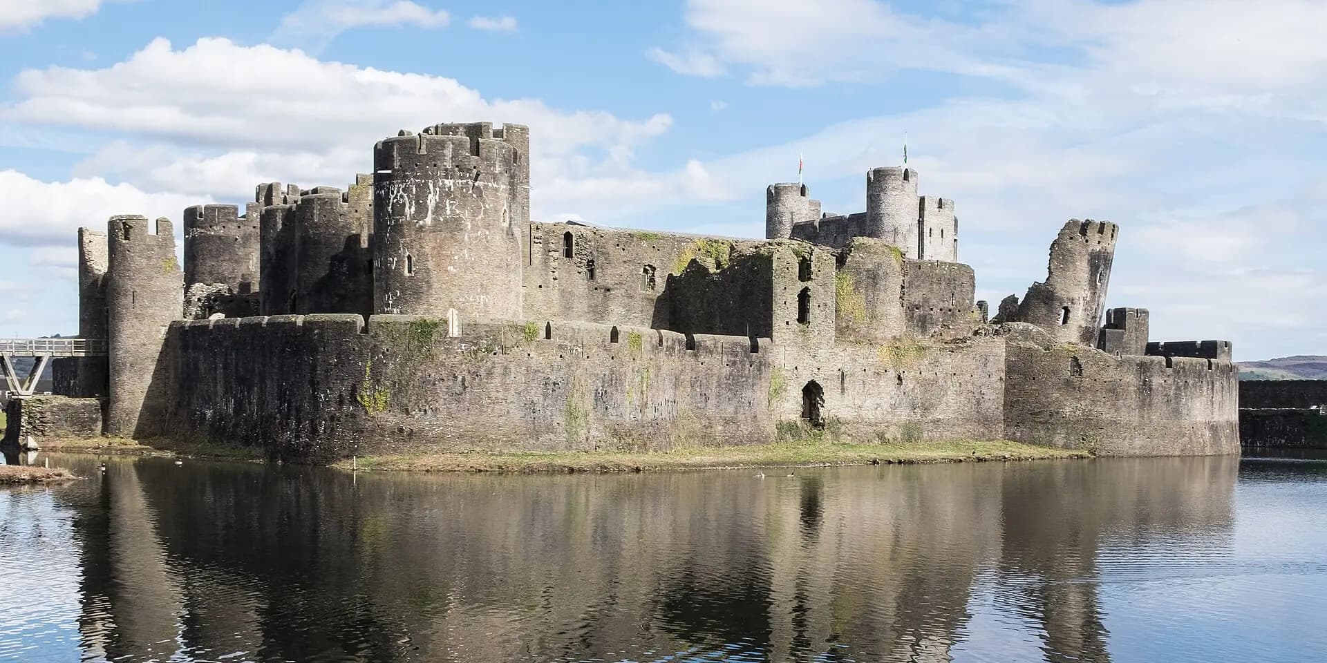 Caerphilly Castle's round towers and walls reflected in the still water of its moat