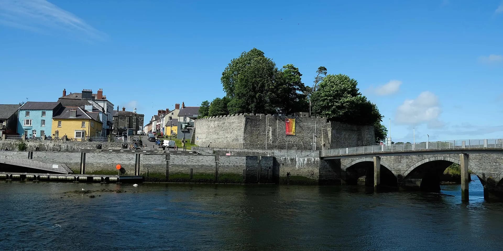Cardigan Castle's walls and the old stone bridge over the River Teifi, with colourful houses beyond