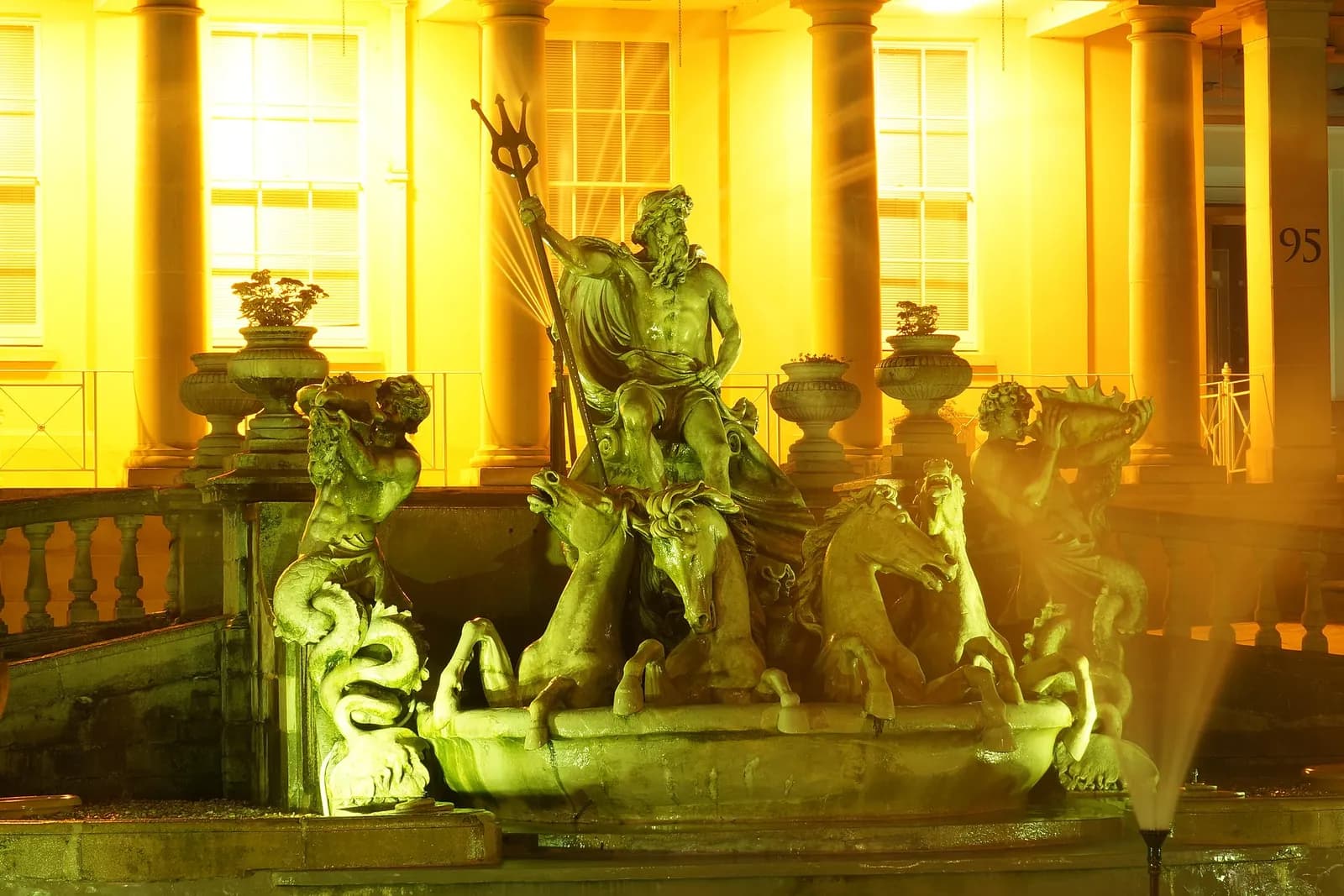 The Neptune Fountain on Cheltenham's Promenade, lit golden at night