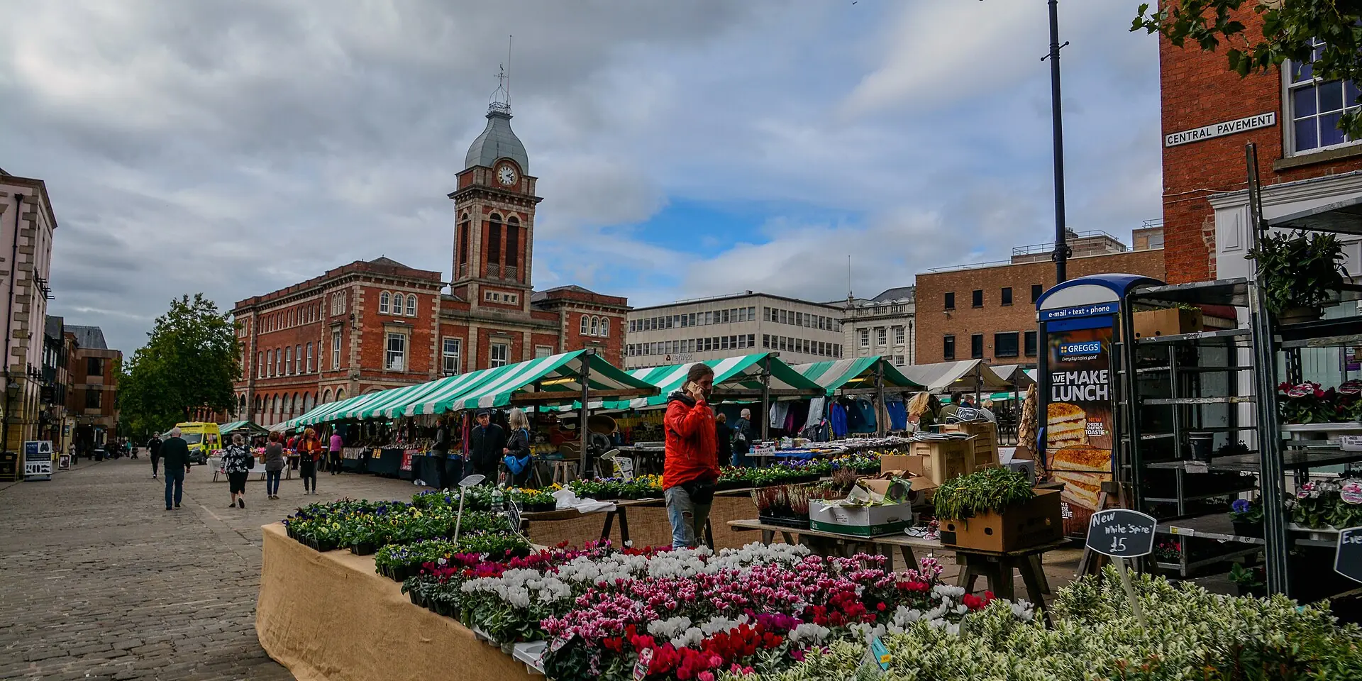 Market stalls and flower displays in Chesterfield's Market Place, with the red-brick Market Hall and its clock tower behind