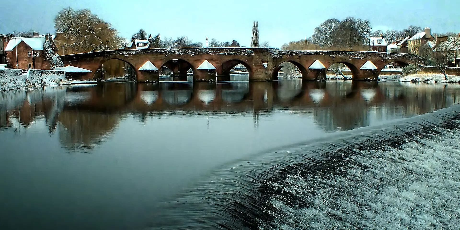 The old stone arches of Devorgilla Bridge over the River Nith in Dumfries, with snow on the banks