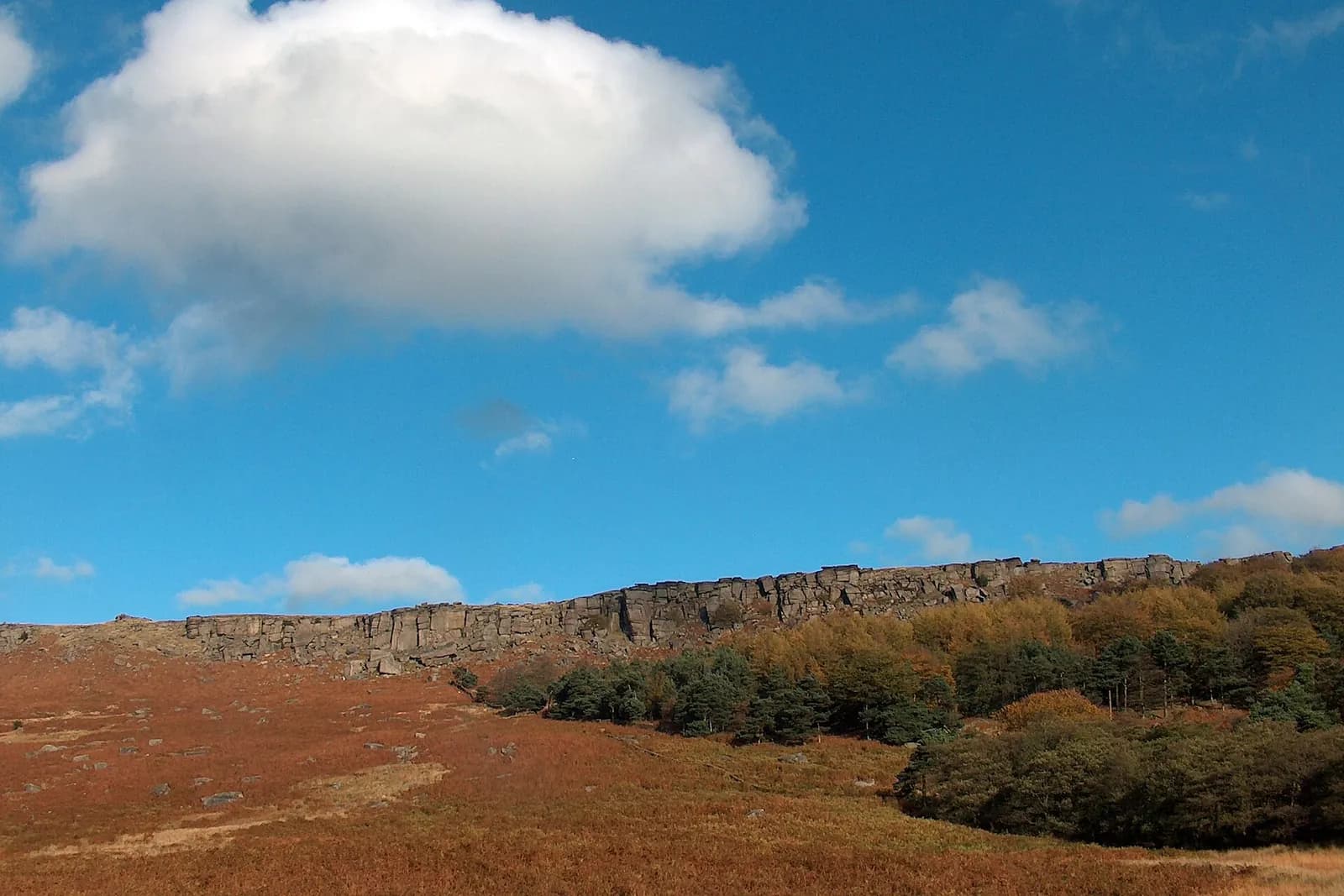 The long gritstone cliff of Stanage Edge above heather moorland under a blue sky