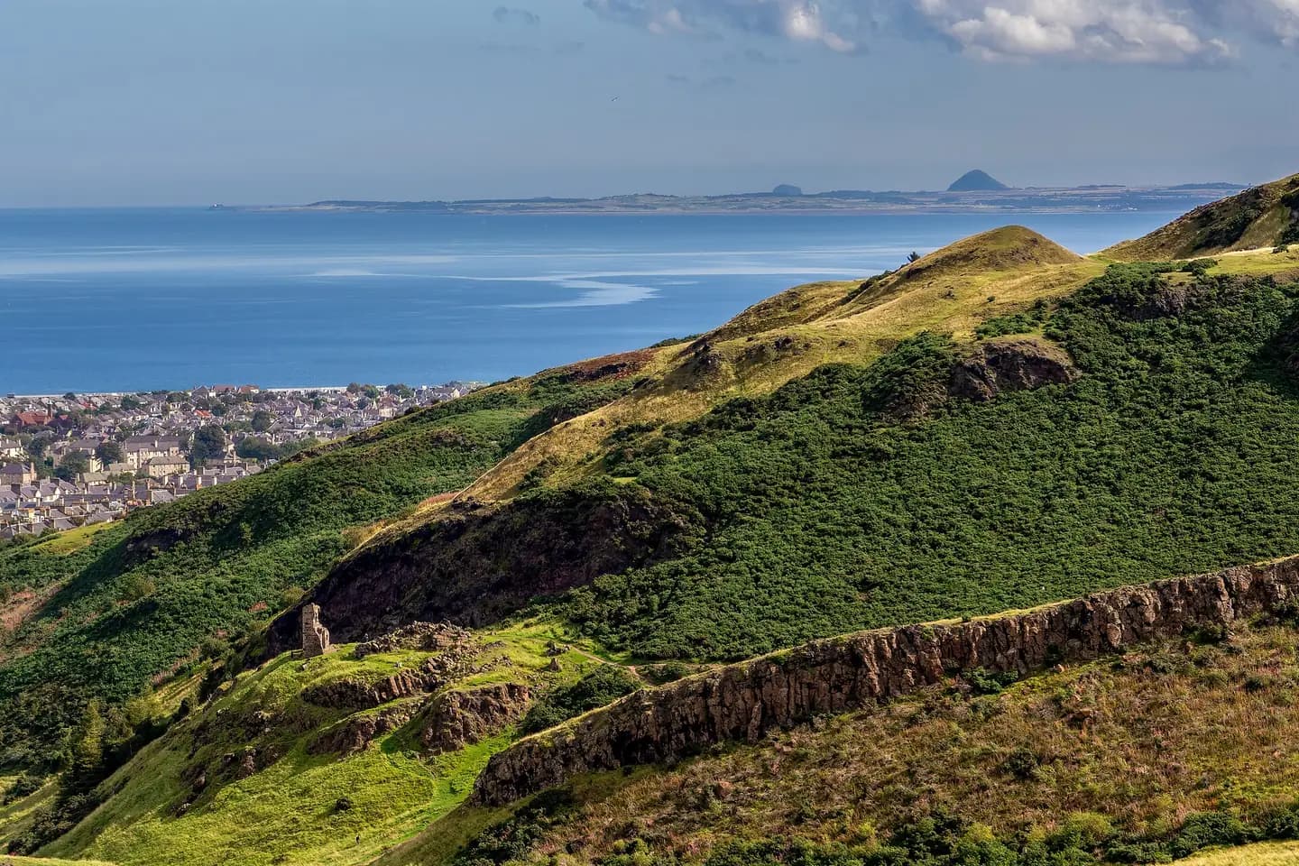 Green slopes of Arthur's Seat above Edinburgh, with the Firth of Forth stretching to the horizon