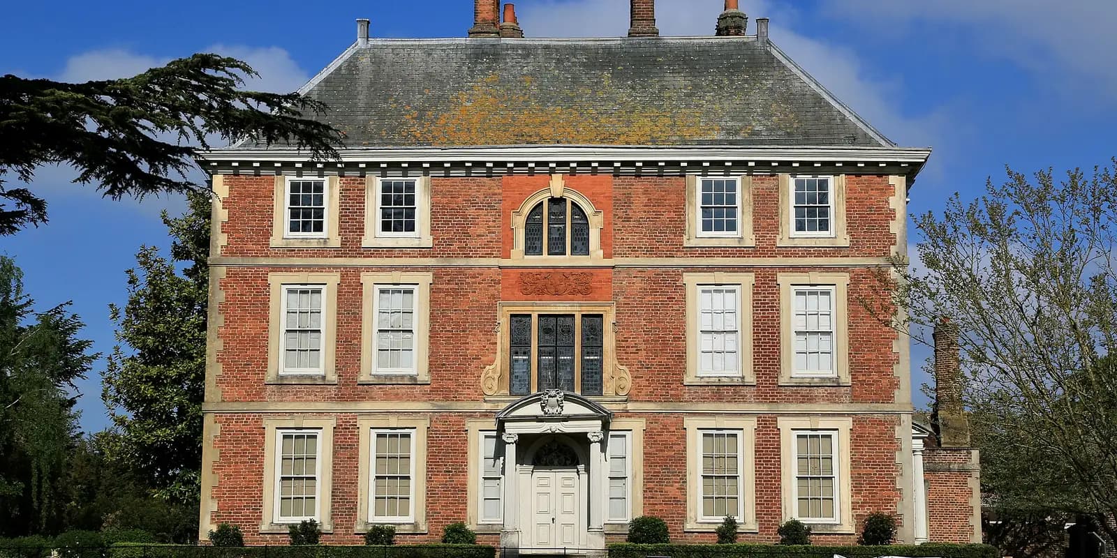 Forty Hall, a red-brick seventeenth-century manor house with white windows, under a blue sky