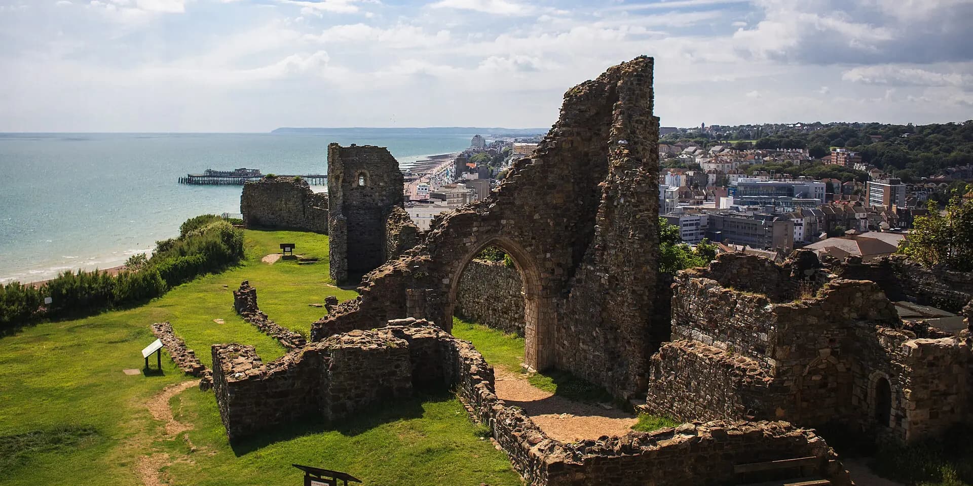 The ruined walls of Hastings Castle on the clifftop, with the town, pier and coast stretching away beyond