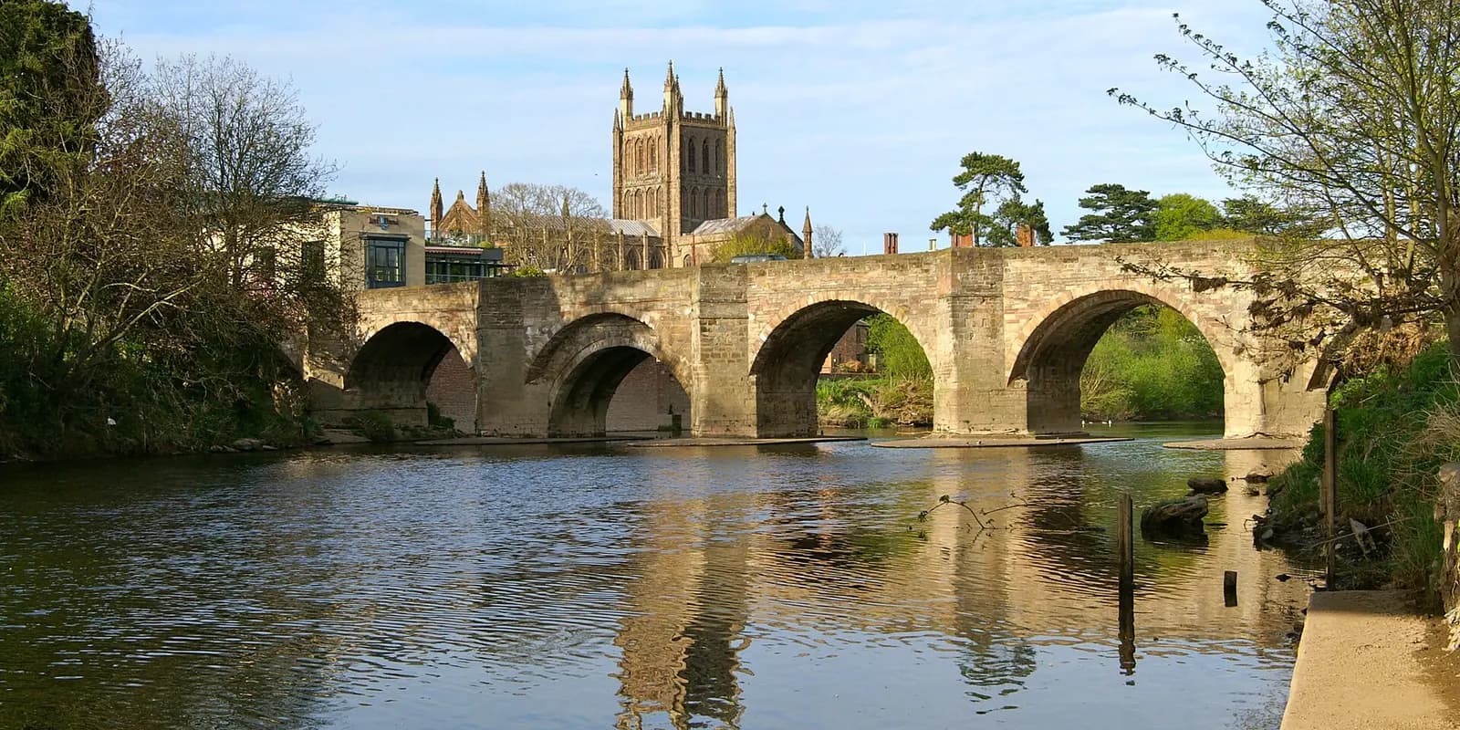 The old stone Wye Bridge reflected in the River Wye, with Hereford Cathedral's tower behind