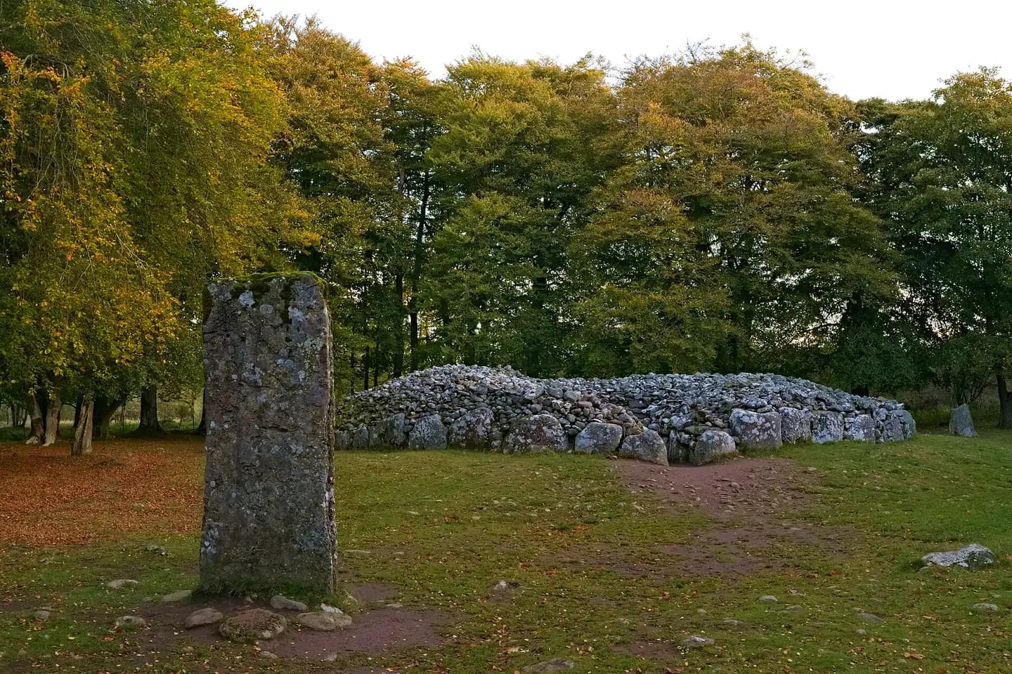 A standing stone and a ring of ancient stone burial cairns among autumn trees at Clava
