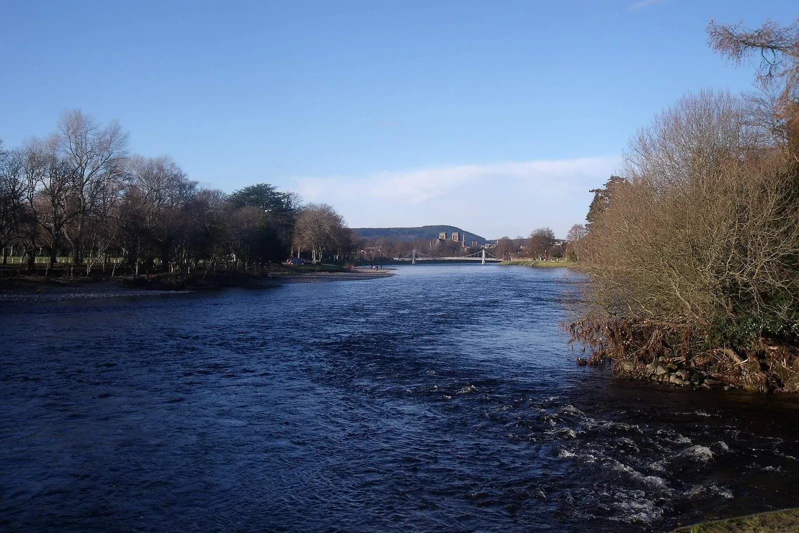 The River Ness flowing past the wooded Ness Islands, with a footbridge in the distance