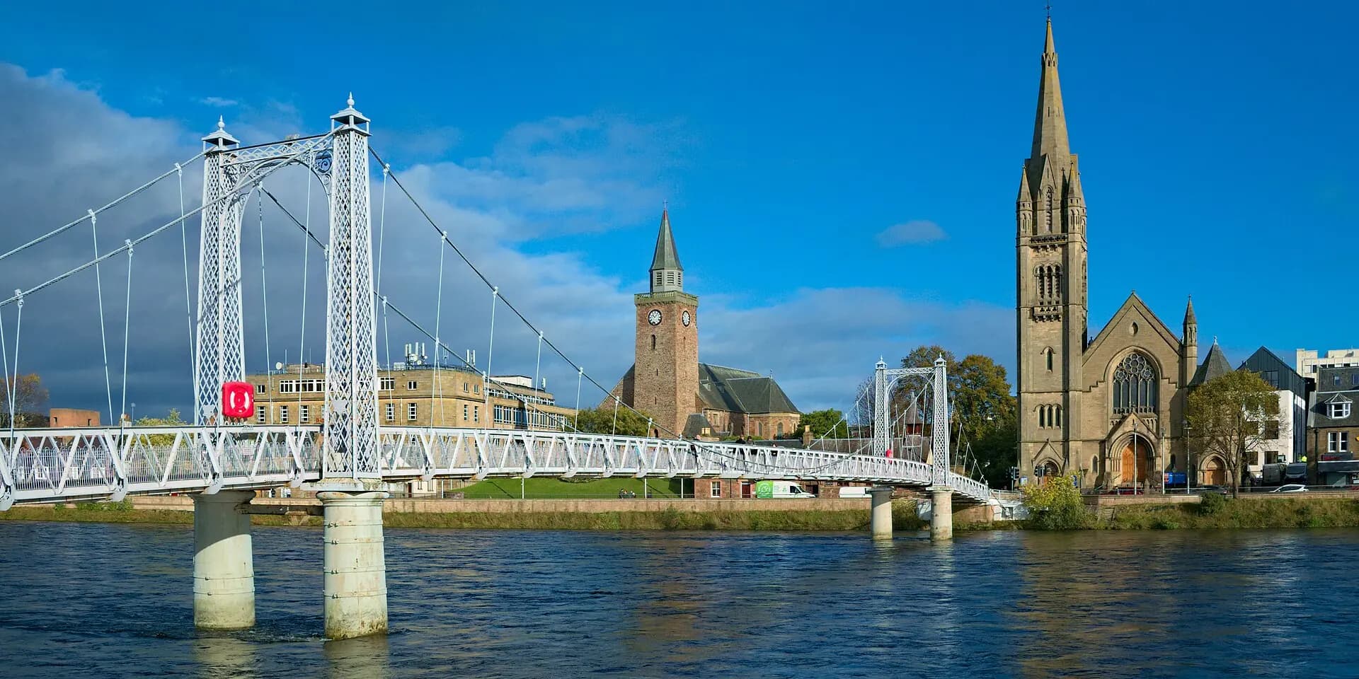 A white footbridge across the River Ness in Inverness, with church spires on the far bank