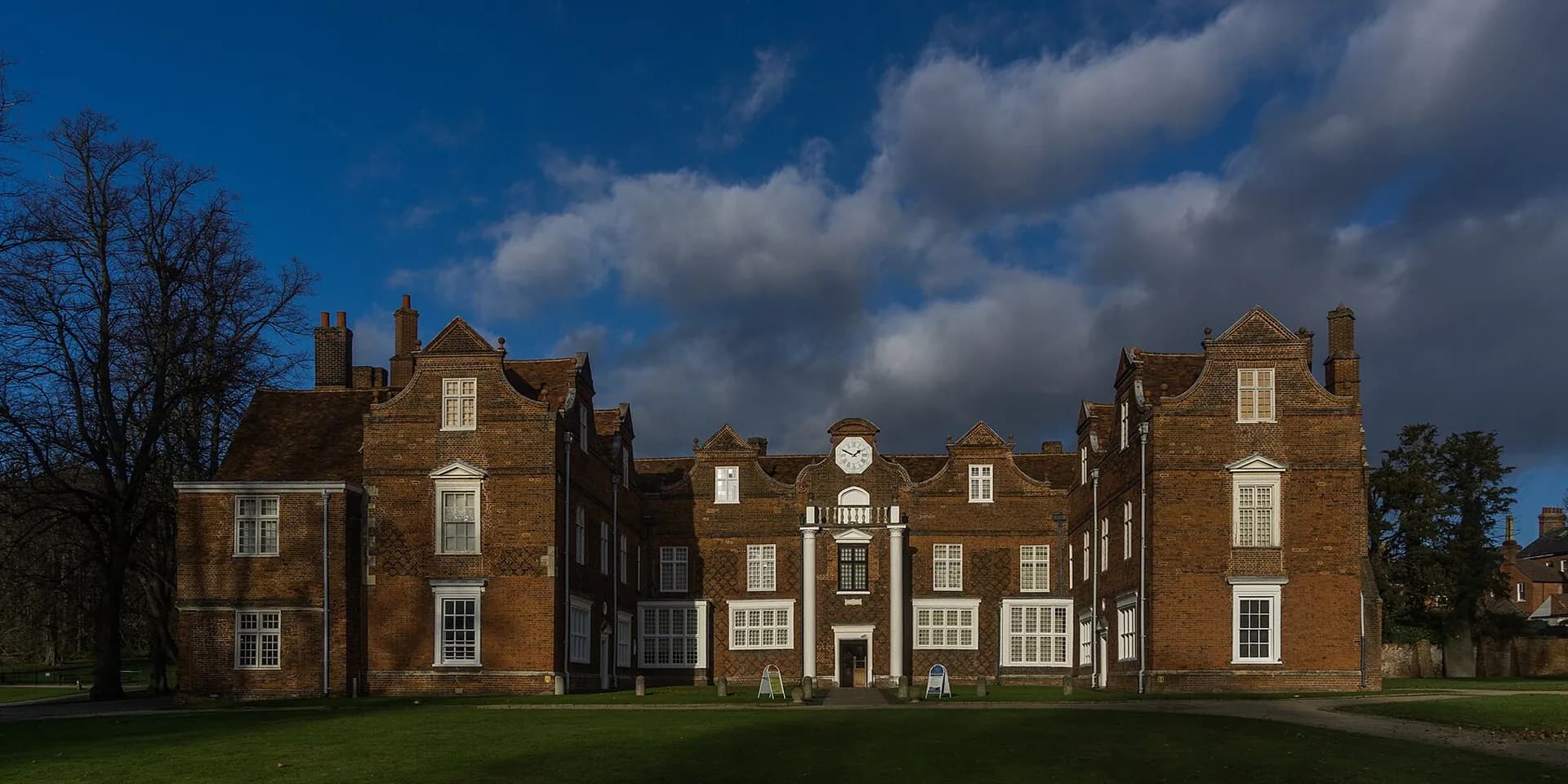 Christchurch Mansion, a Tudor red-brick house with Dutch gables, under a dramatic sky
