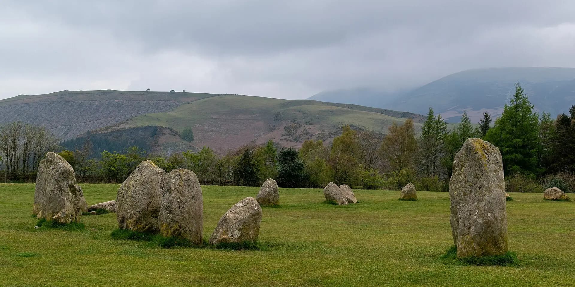 The standing stones of Castlerigg Stone Circle on a green field, with fells rising behind