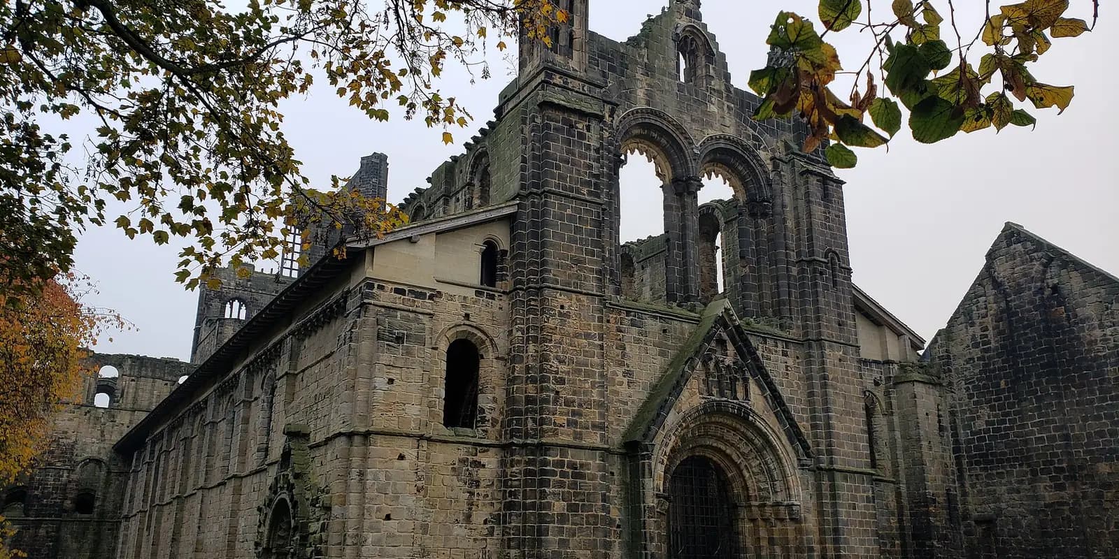 The great stone church of Kirkstall Abbey, roofless and framed by autumn leaves