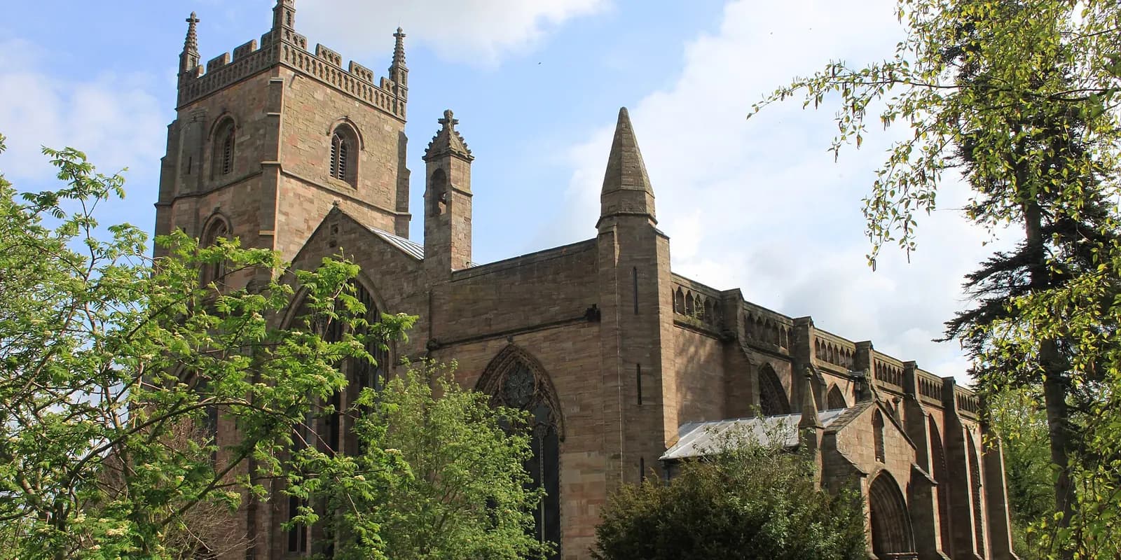 The red sandstone Priory Church of St Peter and St Paul in Leominster, among trees