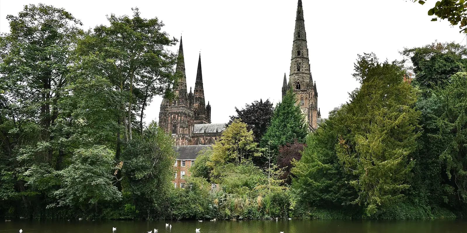 Lichfield Cathedral's three spires rising above trees on the far side of Minster Pool