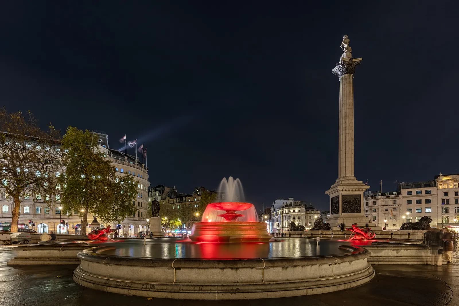 Trafalgar Square at night, with Nelson's Column and a fountain lit up red