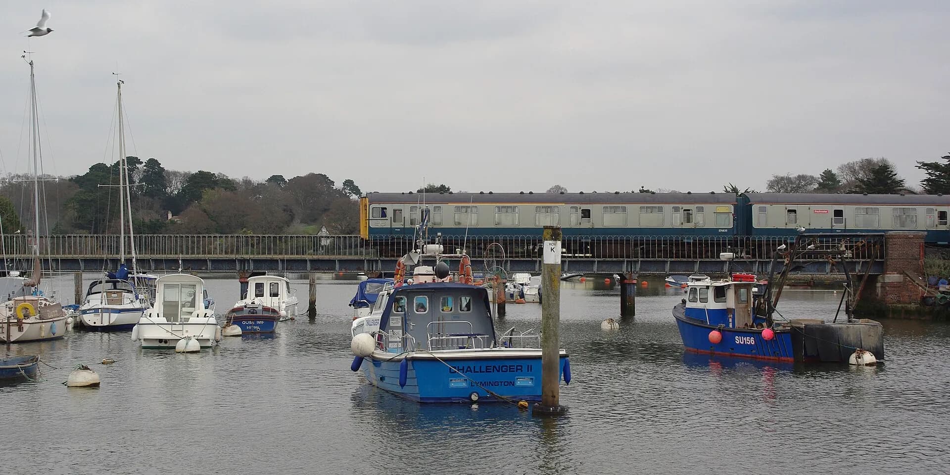 Boats moored in Lymington harbour, with a vintage train crossing the bridge behind