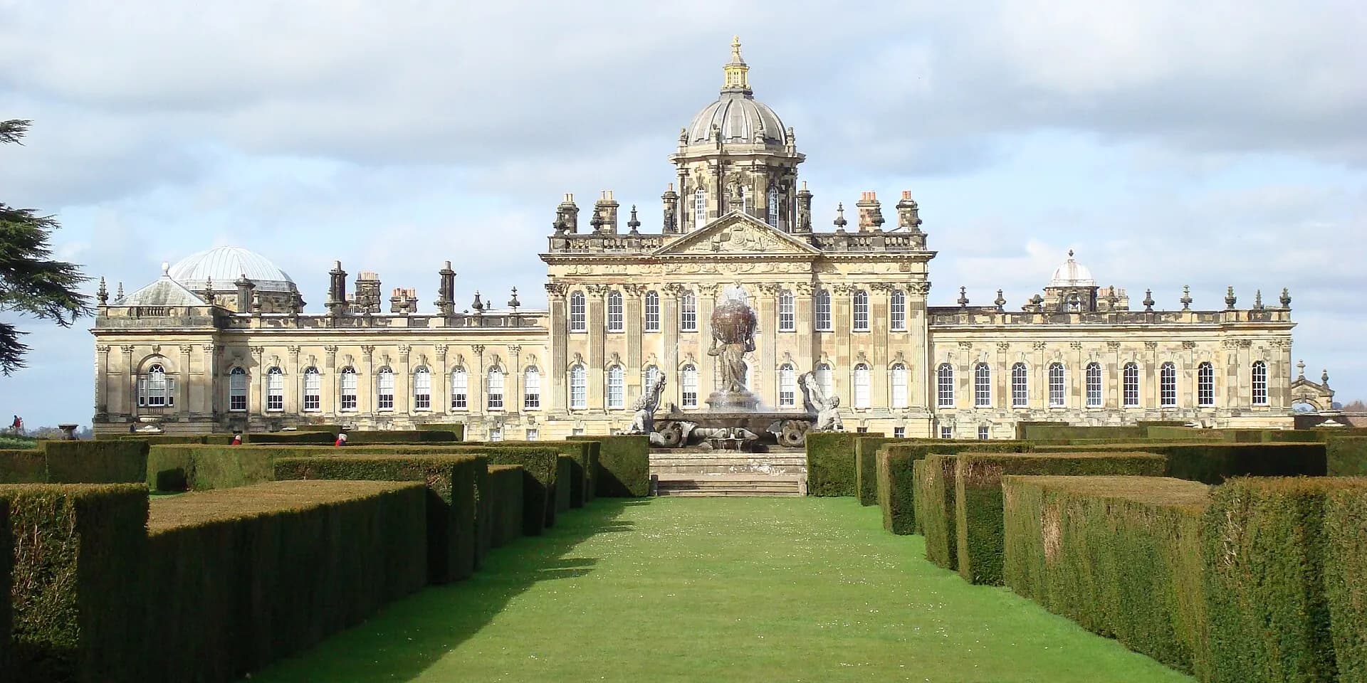 Castle Howard's domed baroque front, seen along a lawn between clipped hedges
