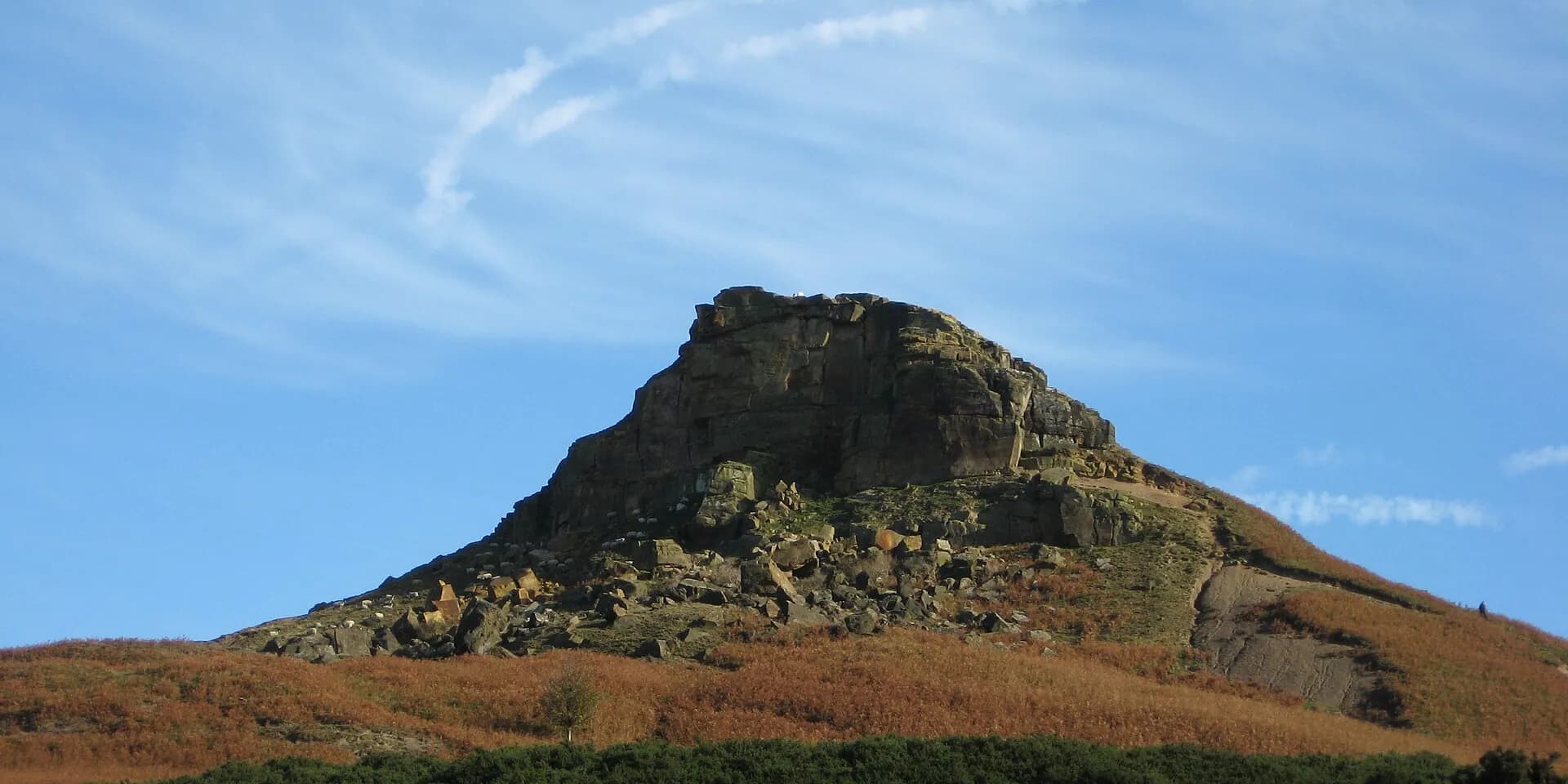 The rocky peak of Roseberry Topping above golden bracken against a blue sky