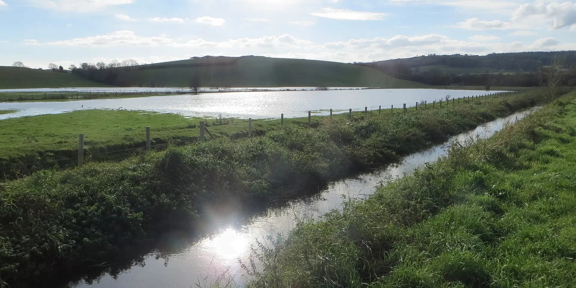The Newry Canal running between green banks, with the sun sparkling on the water and hills behind