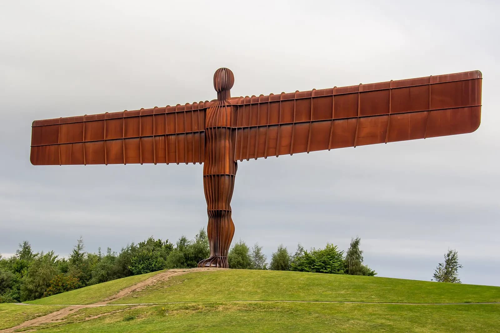 The Angel of the North, a giant rust-red steel sculpture with outstretched wings, on a green hill
