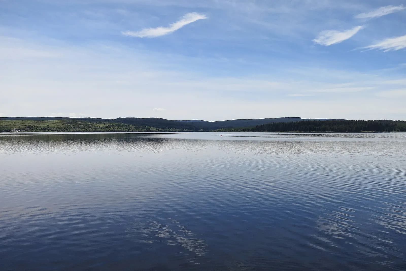 The calm blue water of Kielder Water stretching to forested hills under a wide sky