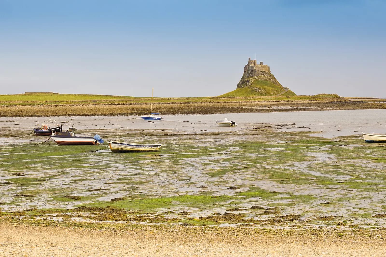 Lindisfarne Castle on its rocky crag across the mudflats of Holy Island, with small boats at low tide