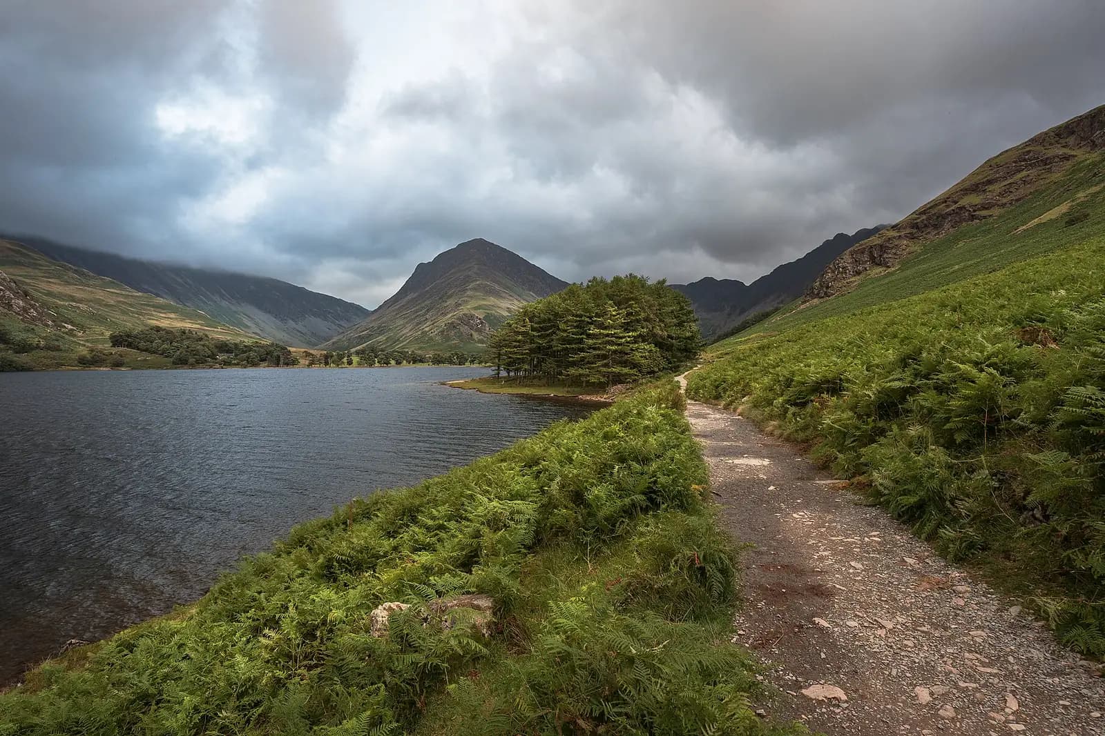 A path along the shore of Buttermere towards the peak of Fleetwith Pike, under a stormy sky