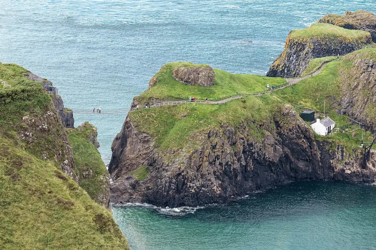 The Carrick-a-Rede rope bridge strung between green cliffs above turquoise sea