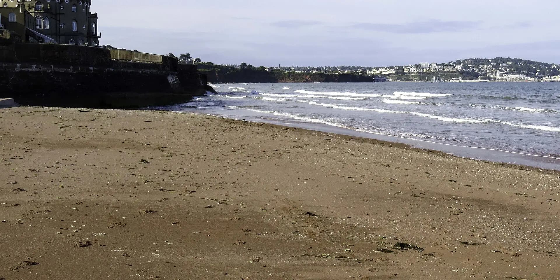 Paignton's sandy beach with waves rolling in and the curve of Tor Bay beyond