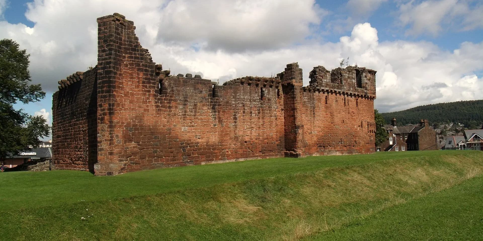 The red sandstone ruins of Penrith Castle above a grassy moat under a cloudy sky
