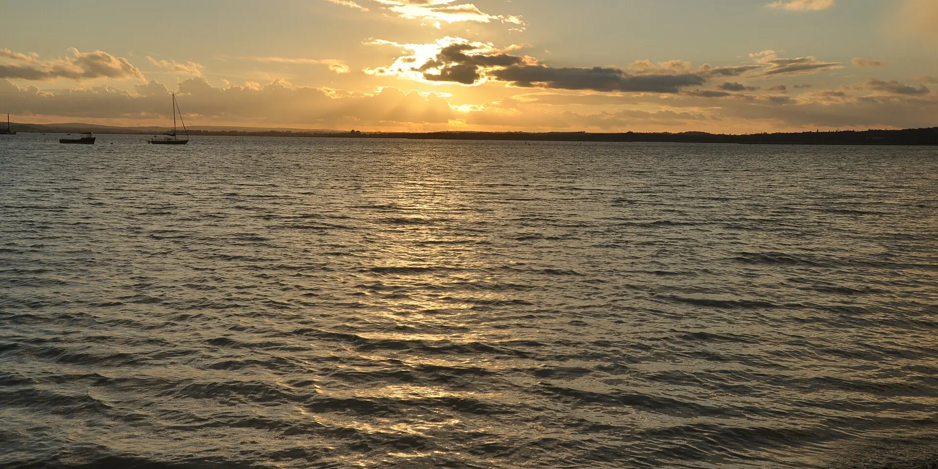 Golden sunset light on the calm water of Poole Harbour, with small boats at anchor