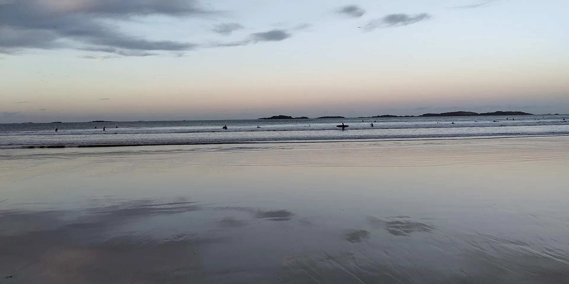The wide sands of East Strand in Portrush at dusk, with surfers in the shallow waves