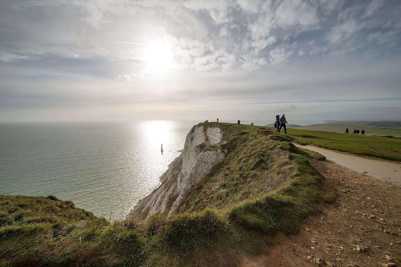 Walkers on the clifftop at Beachy Head, with sunlight on the sea below the chalk cliffs