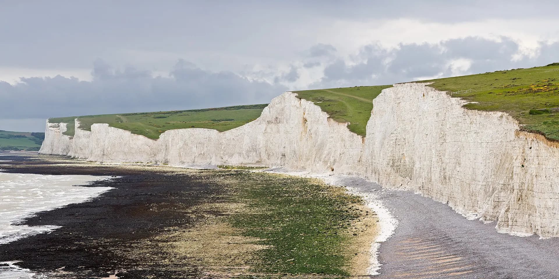 The white chalk cliffs of the Seven Sisters rising above a shingle beach, with green downland on top