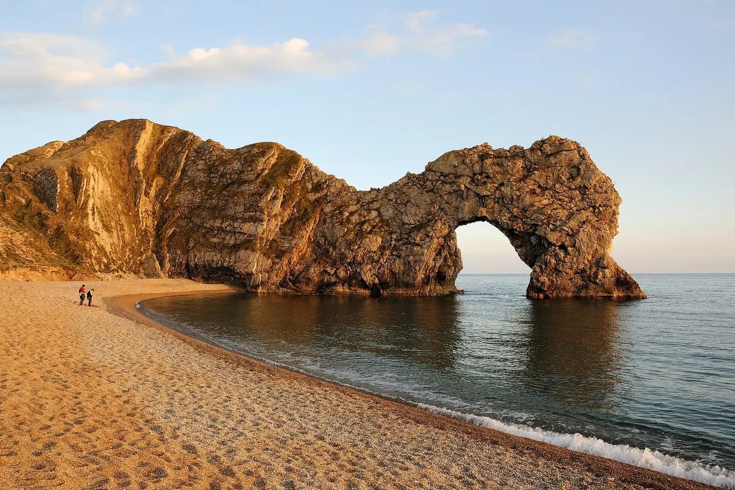 Durdle Door's limestone arch glowing in the evening sun above a curving shingle beach