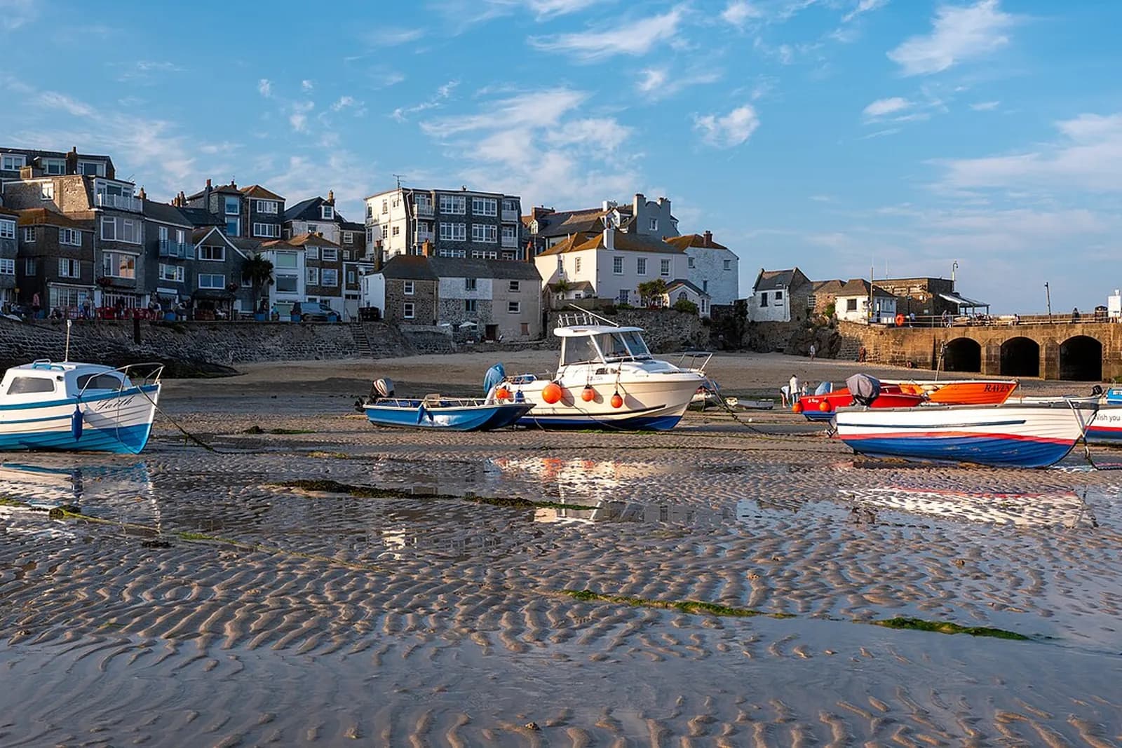 Small boats resting on the sand in St Ives harbour at low tide, below the town's white houses