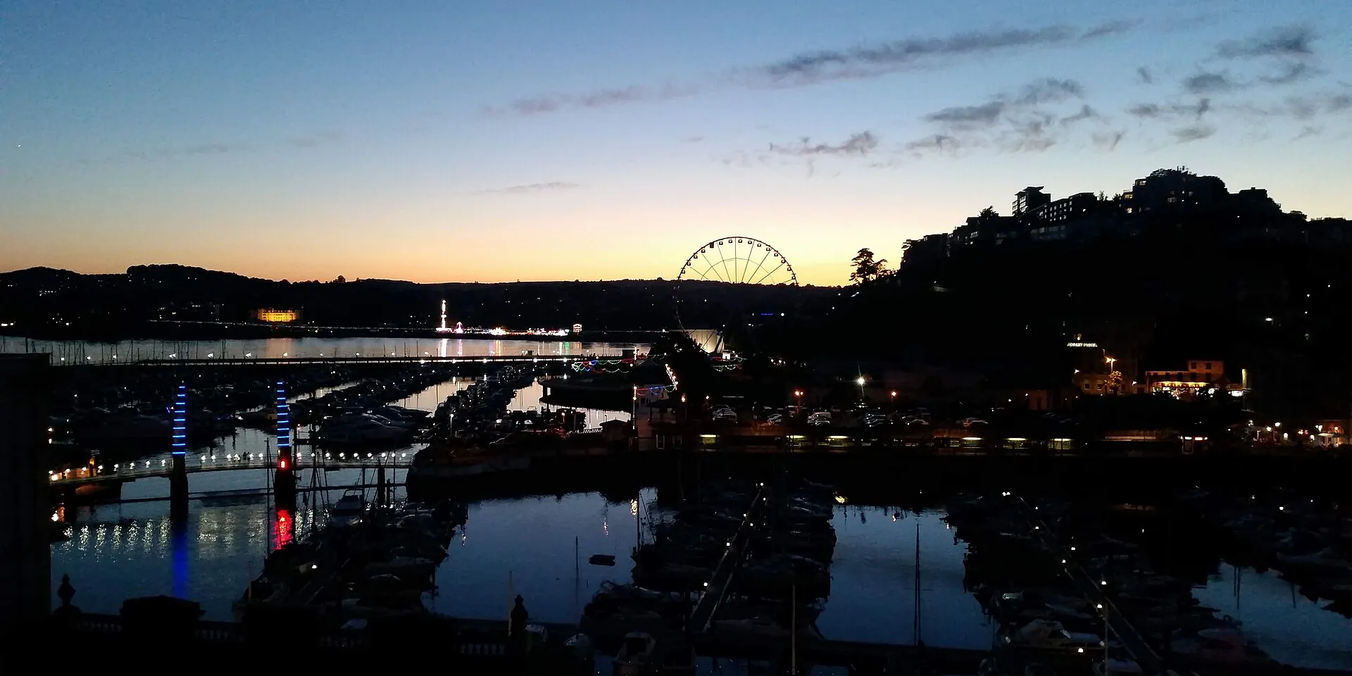 Torquay harbour at dusk, with lights reflected in the water and the big wheel on the skyline