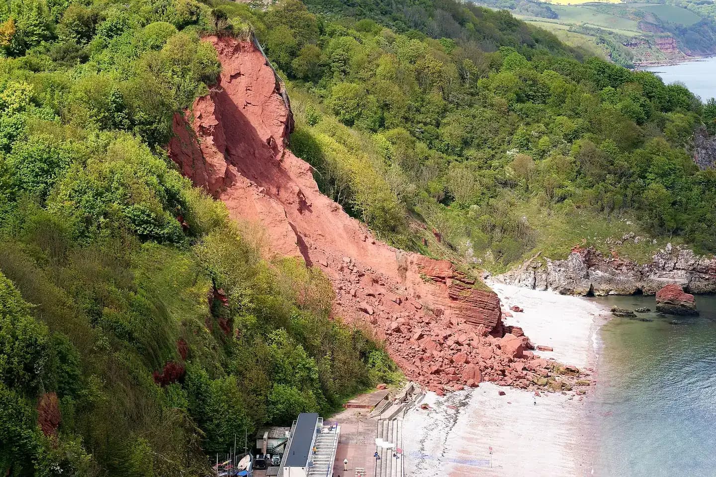 Oddicombe beach below steep wooded cliffs, with a scar of red rock where the cliff has slipped