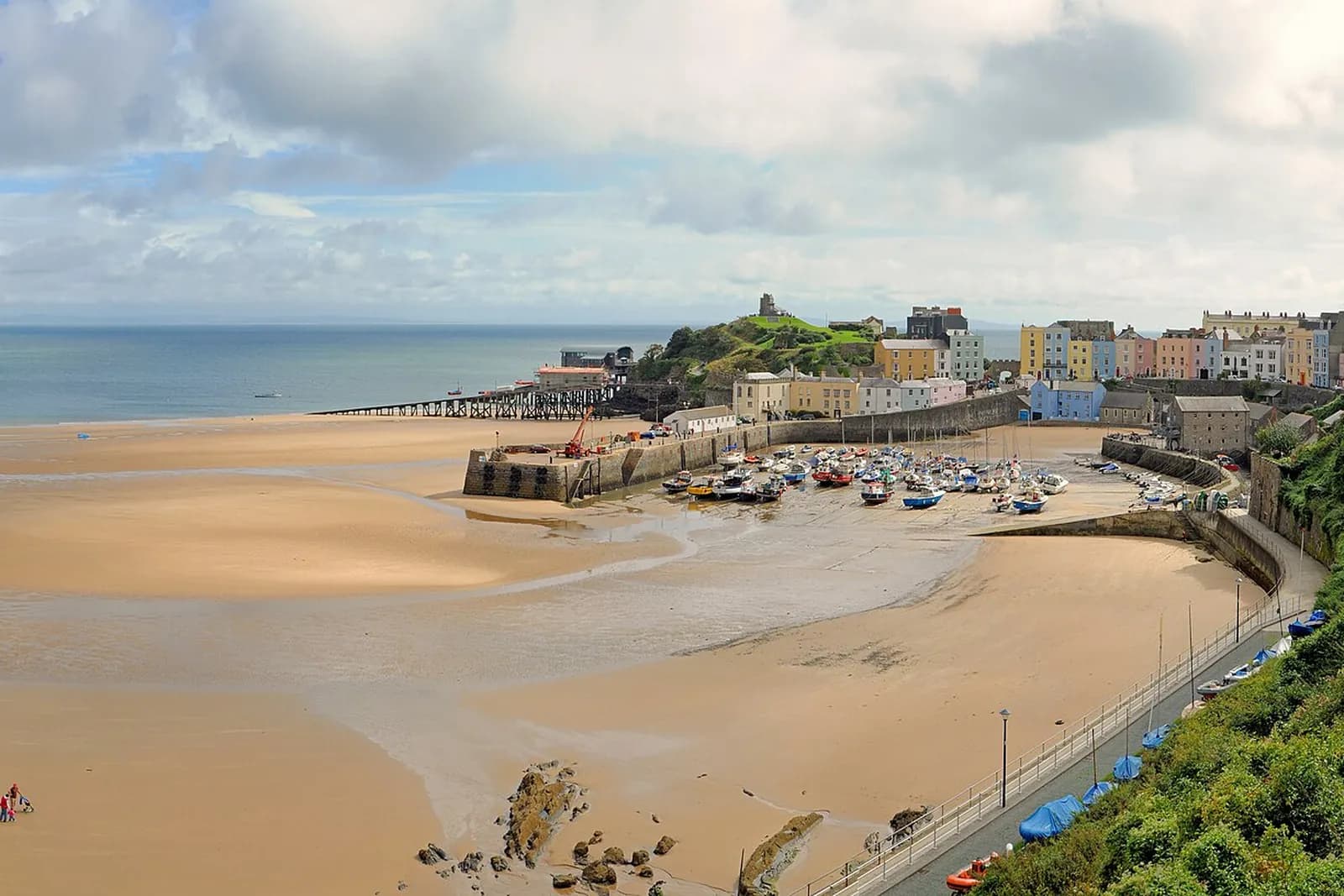 Tenby harbour at low tide, with colourful houses along the clifftop and boats on the sand