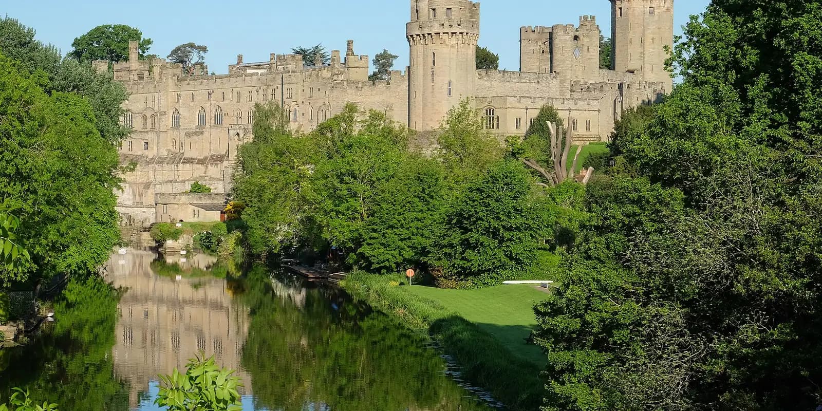 Warwick Castle above the River Avon, framed by green trees