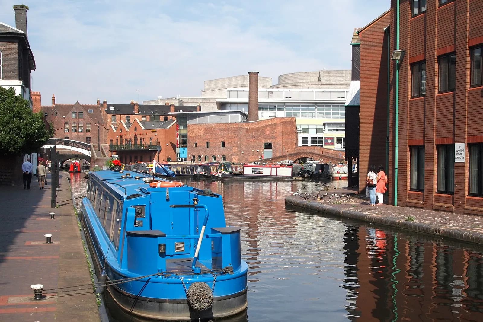 A bright blue narrowboat moored at Gas Street Basin in Birmingham, among brick canalside buildings