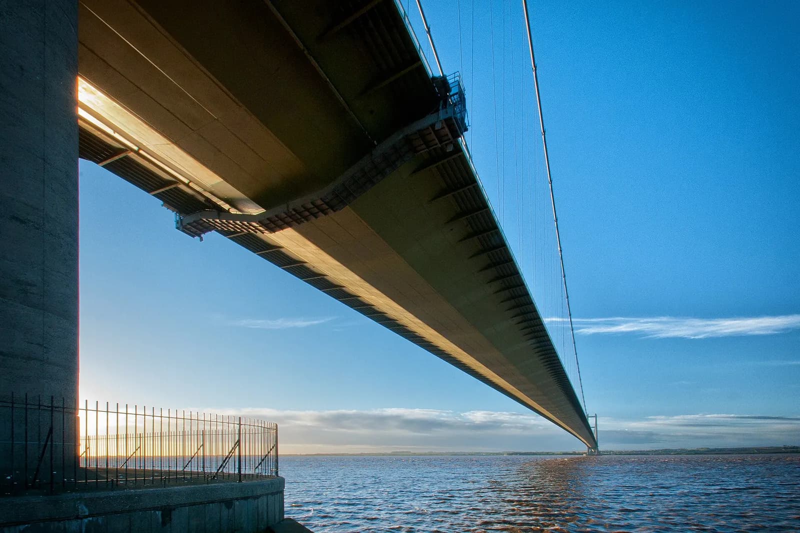 Looking up at the underside of the Humber Bridge as it stretches across the estuary under a blue sky